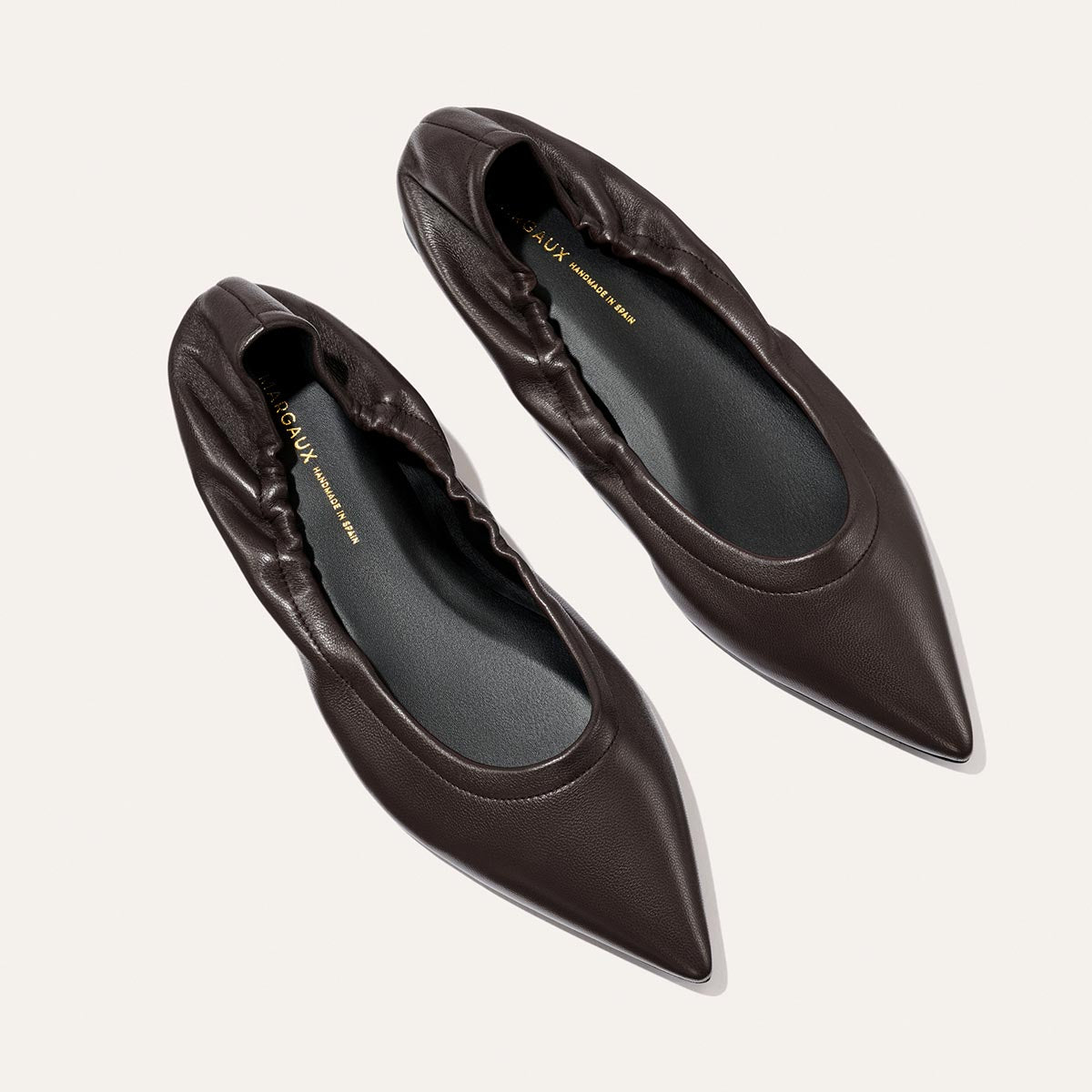 A pair of The Roma - Espresso Nappa pointed-toe ballet flats by Margaux, featuring a sophisticated dark brown hue and elasticized backs, displayed from above on a light background.