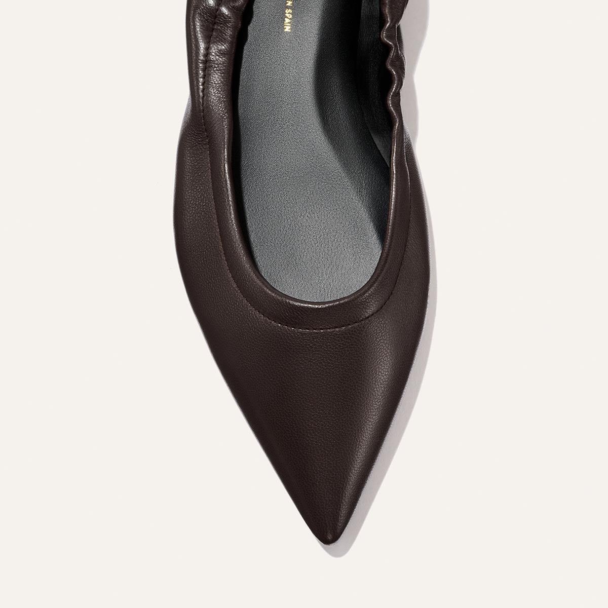 Close-up of The Roma - Espresso Nappa, a dark brown pointed-toe ballet flat by Margaux featuring gathered detailing along the edges, set against a light background.