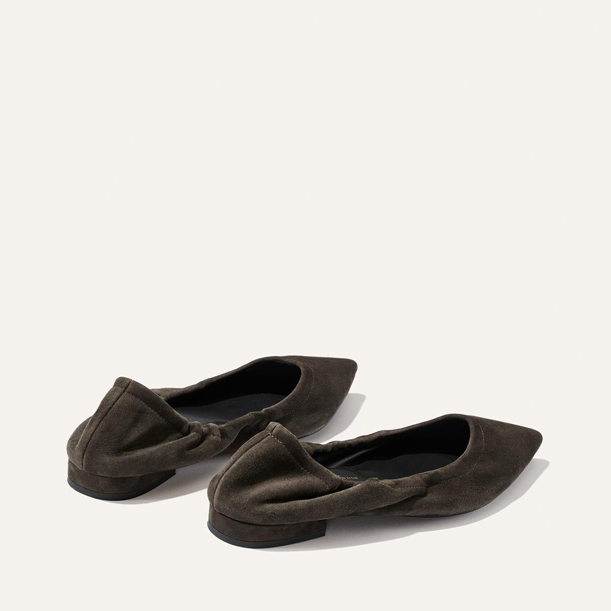 The Roma – Graphite Suede by Margaux, a sophisticated ballet flat crafted in dark grey suede with a pointed toe and elegant ruched detailing on the sides, is displayed on a light background.