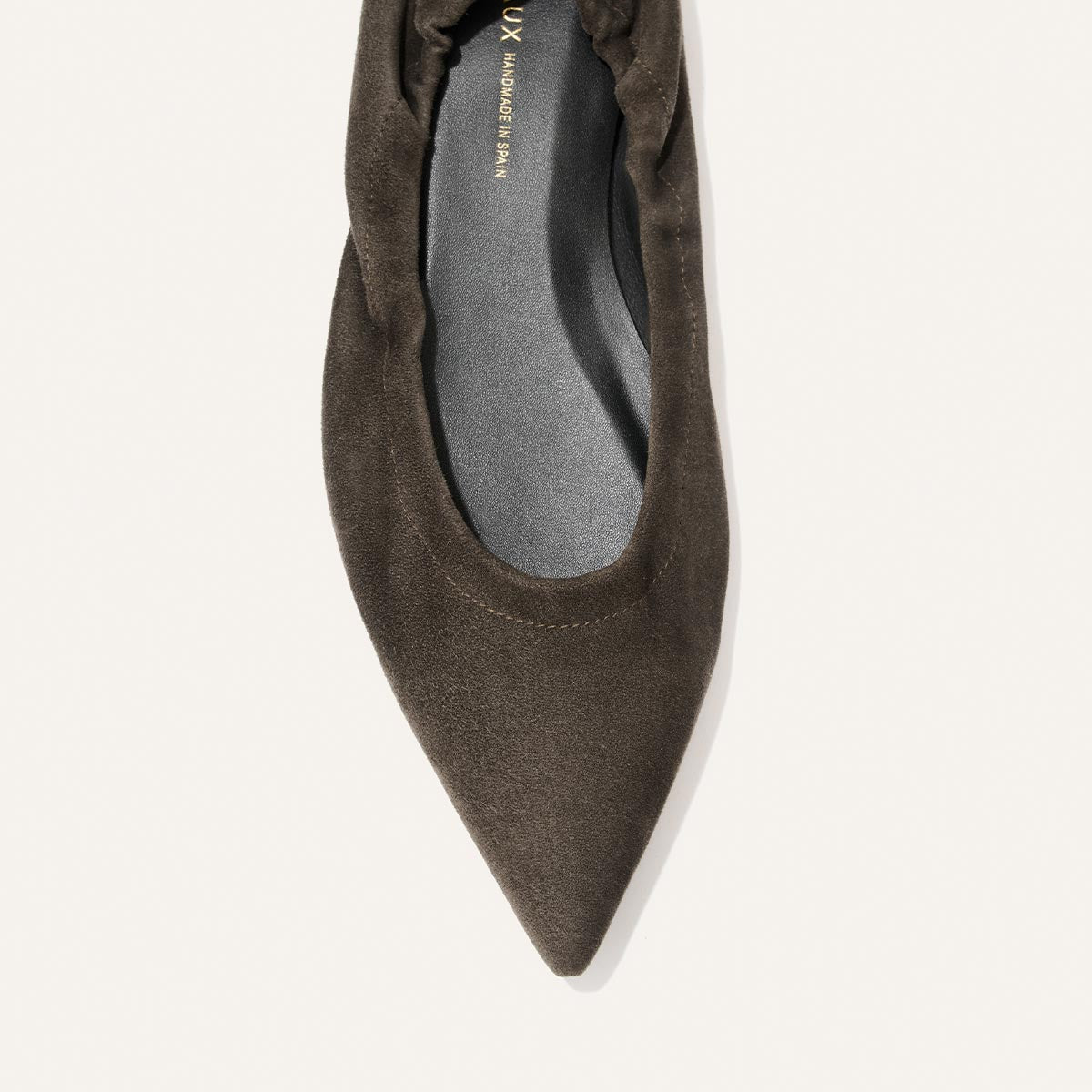 Close-up of the front of The Roma - Graphite Suede by Margaux, a dark brown suede pointed-toe ballet flat featuring a gathered, ruched edge and a black insole, displayed on a white background.