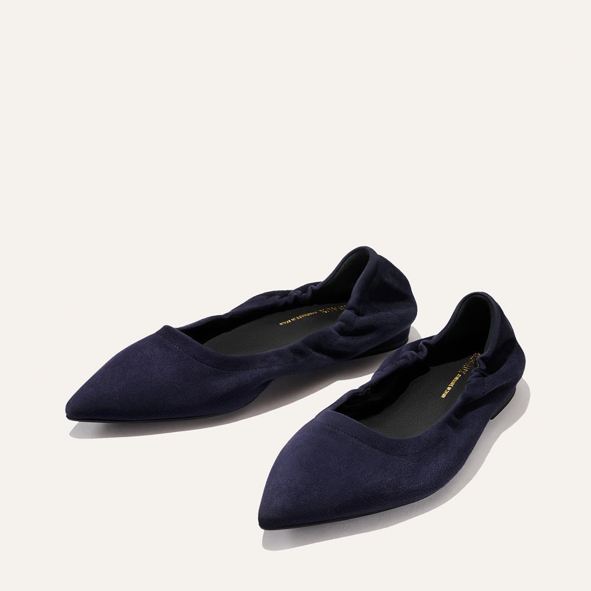 A pair of Margaux's The Roma - Indigo Suede pointed-toe ballet flats, featuring gathered detailing at the sides, is displayed on a light background.