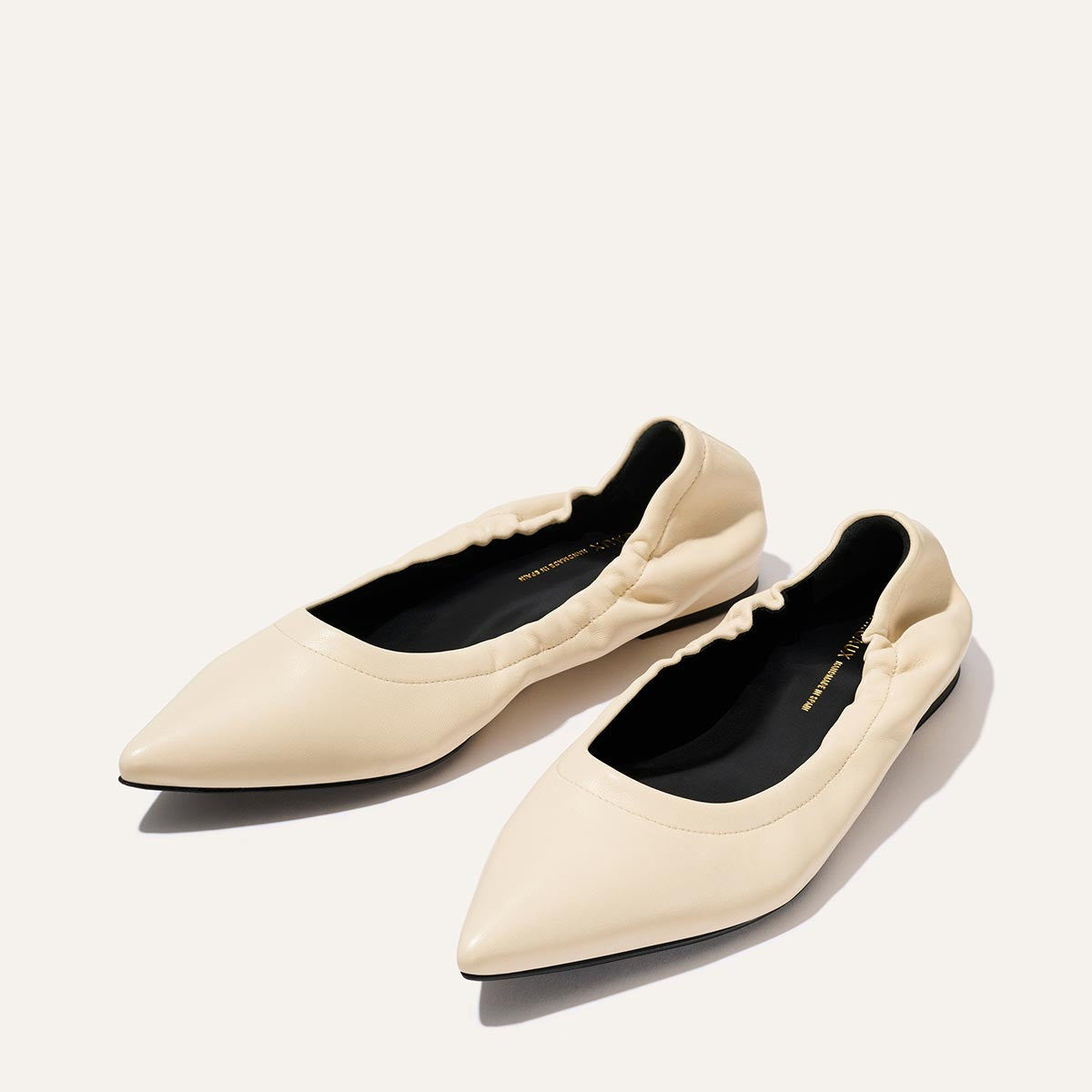 The Margaux Roma - Ivoire Nappa are cream-colored, pointed-toe ballet flats with subtle ruching around the opening, shown on a light background.