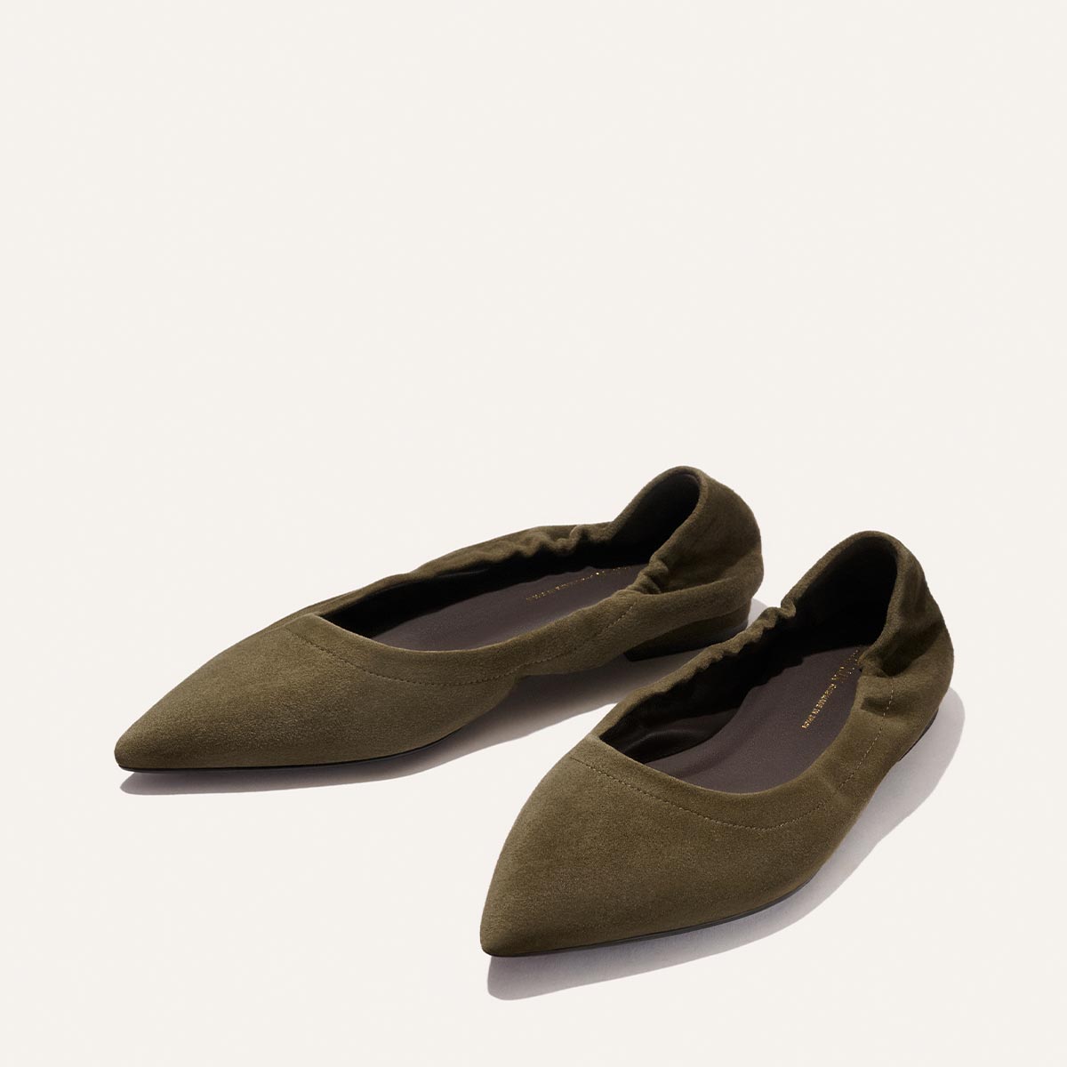 A pair of Margaux's The Roma - Moss Suede pointed-toe ballet flats with ruched heel detail, displayed on a plain, light background.