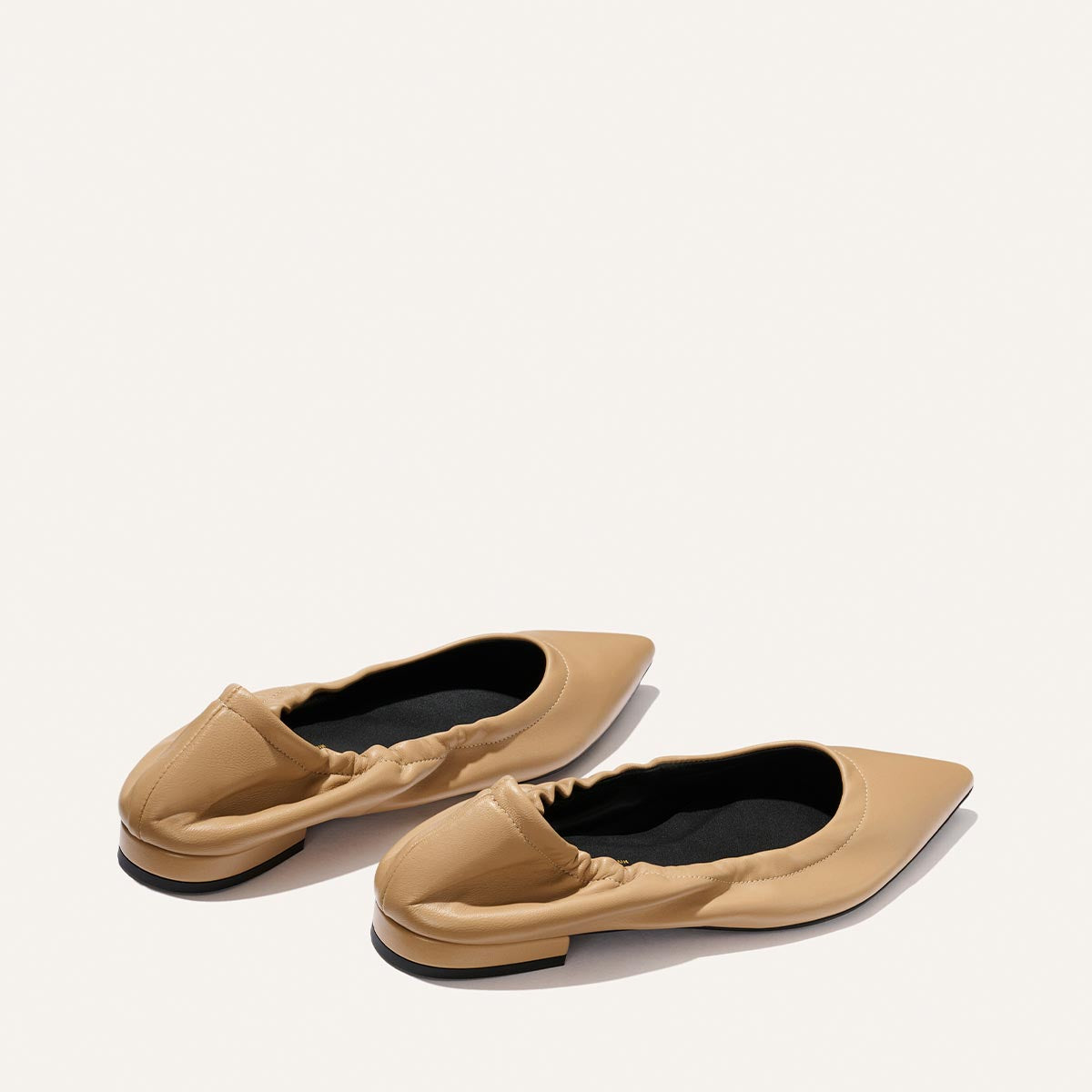 The Roma - Praline Nappa by Margaux: tan pointed-toe flats with elasticized edges and black insoles, shown on a light background.
