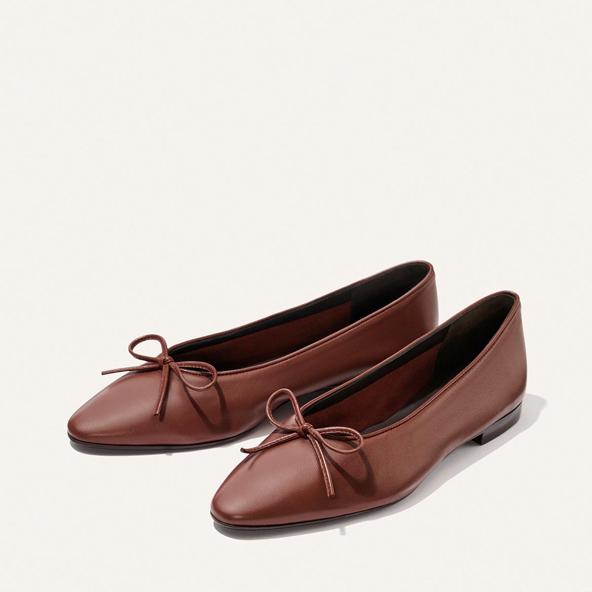 The Salamanca - Brandy Nappa by Margaux: brown pointed-toe flats with thin front bows, low heels, and a simple, elegant design in buttery soft leather. Displayed on a plain light background.