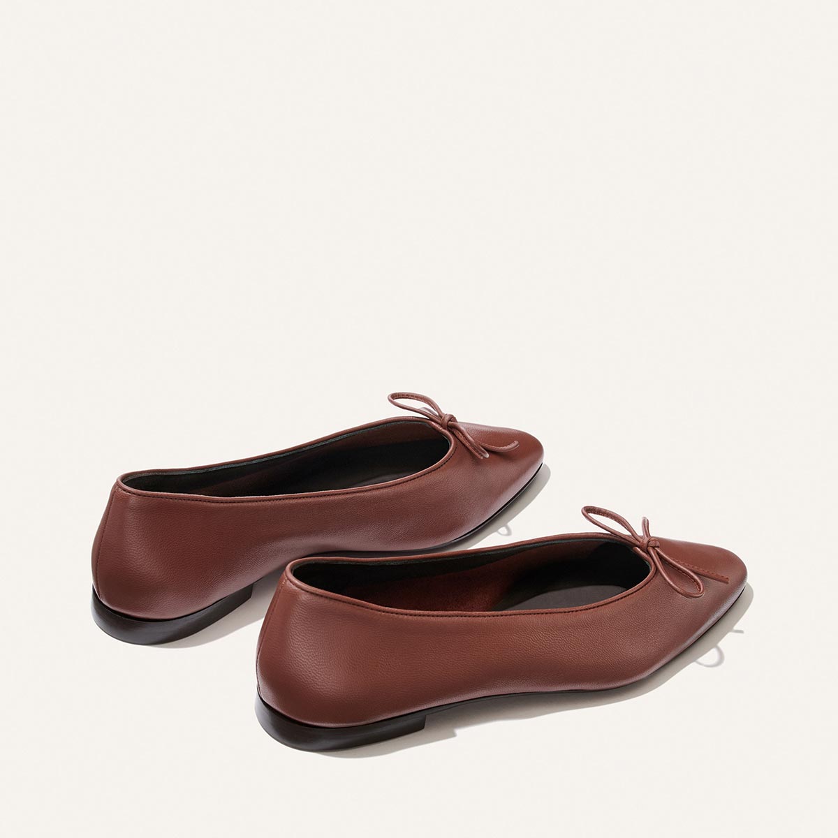 The Salamanca - Brandy Nappa by Margaux features brown pointed-toe flats with small bows, made from buttery soft leather and shown side by side on a light, plain background.