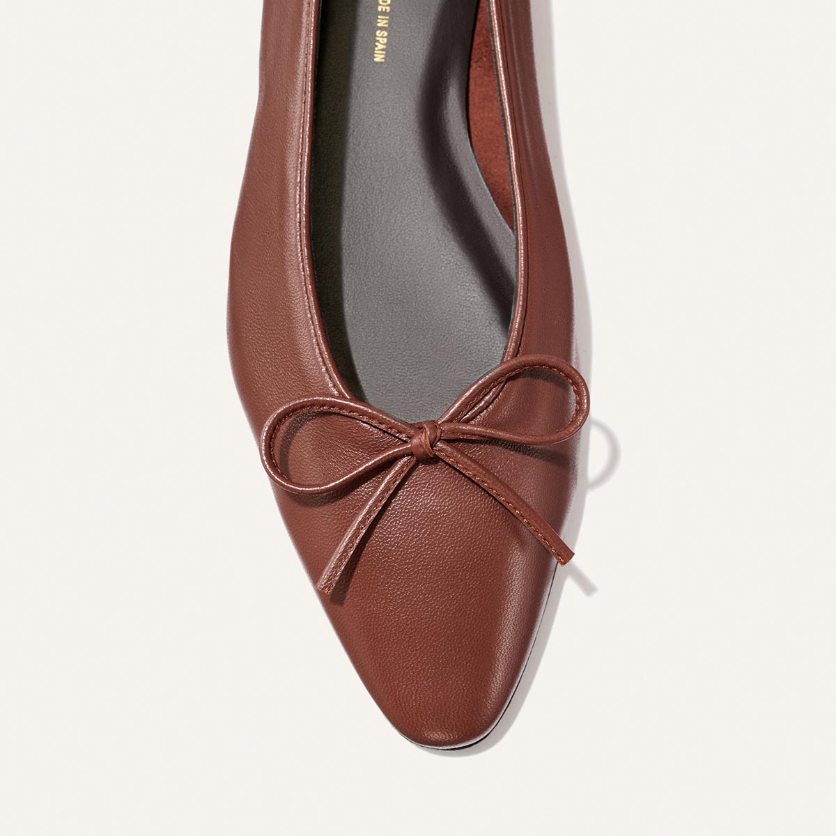 A close-up of Margaux’s The Salamanca - Brandy Nappa, a buttery soft leather pointed-toe flat with a bow detail, shown from above against a light background.