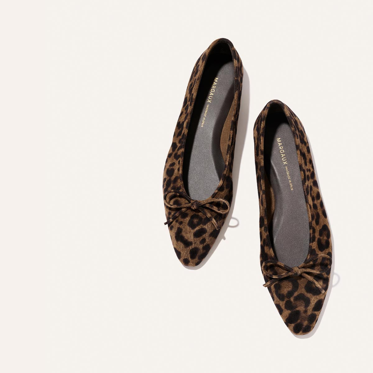 A pair of Margaux's The Salamanca - Brown Leopard Suede flats, featuring a pointed toe, brown and black leopard print suede, and small bows on the front, displayed on a light background.