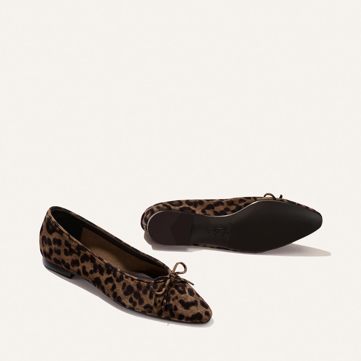 Two pairs of The Salamanca - Brown Leopard Suede by Margaux are displayed on a white background—one upright with a small bow, the other revealing the unlined construction and sole.