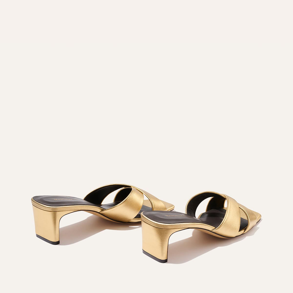 The Selene 50 - Gold Nappa by Margaux: gold open-toe heeled sandals with crisscross leather straps and sturdy block heels, displayed on a neutral background.