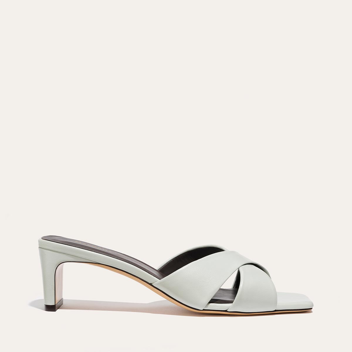 The Selene 50 - Sky Nappa by Margaux is a light gray heeled sandal with a low square block heel and open toe. It features two wide, crisscrossed leather straps over the foot and is displayed on a plain white background.