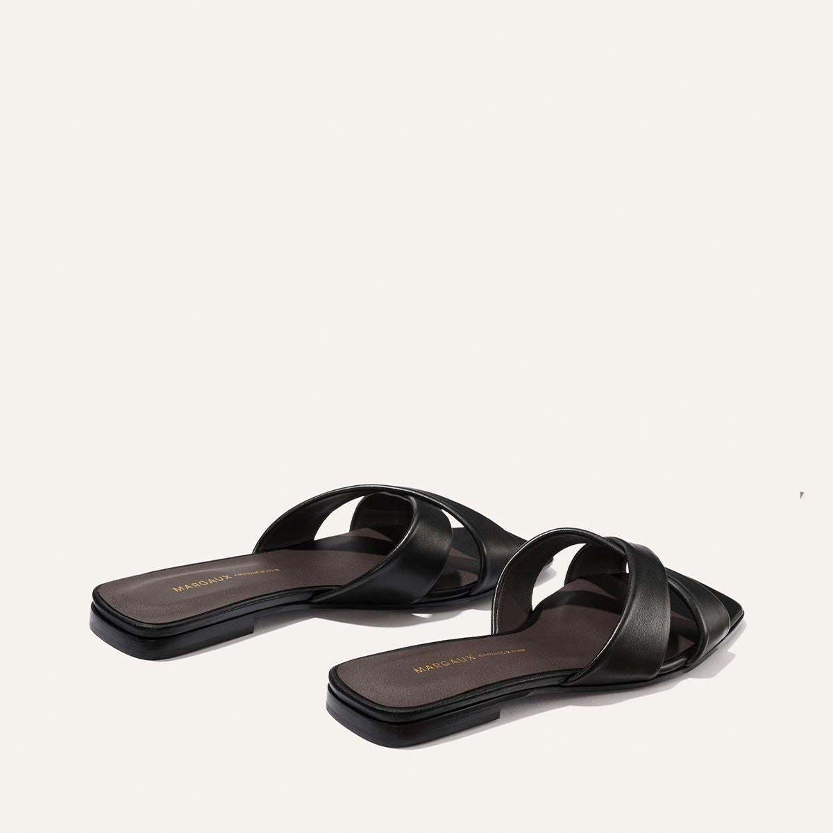 The Selene Flat Sandal by Margaux features black nappa leather, crisscross straps, flat soles, and square toes. Displayed on a plain white background.