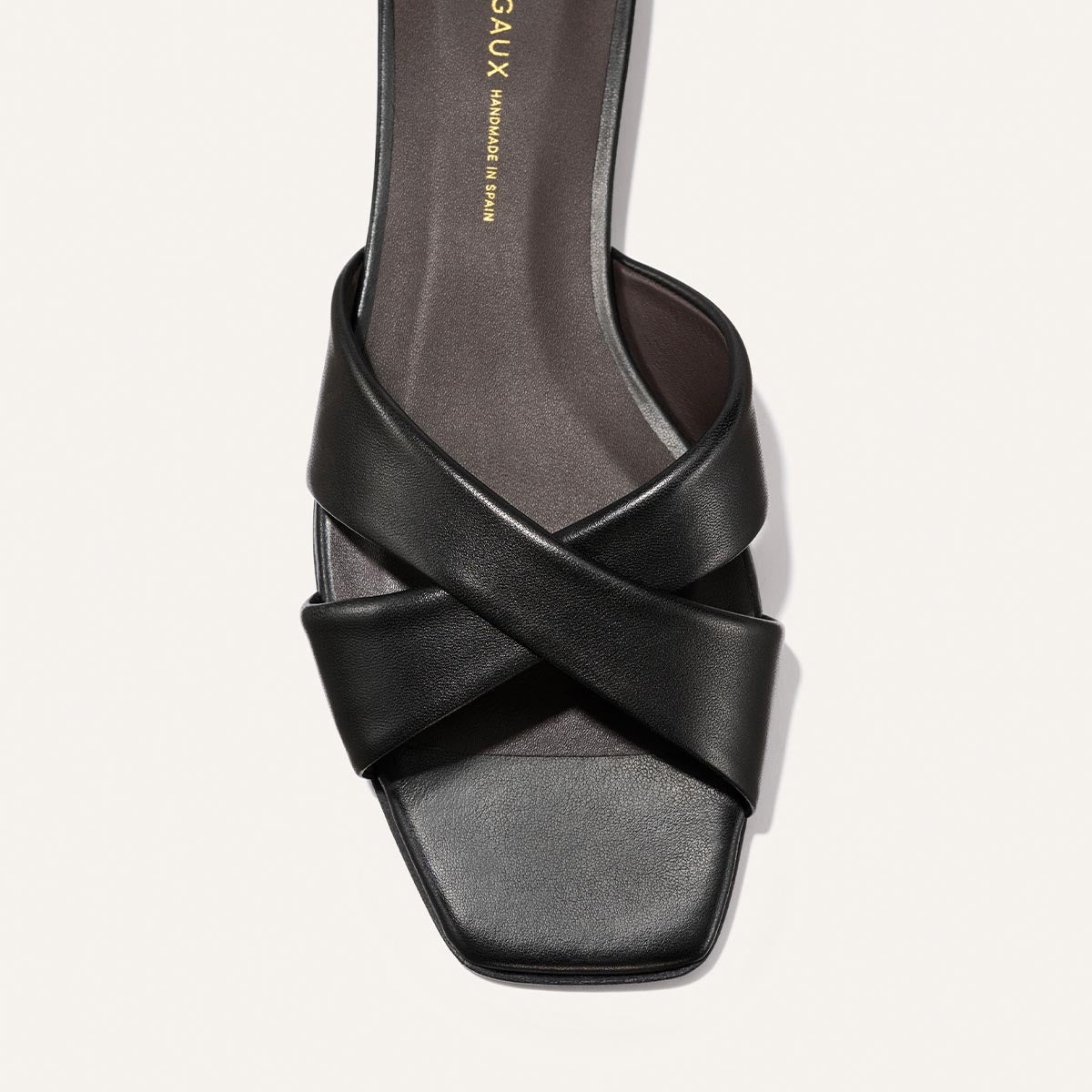 The Selene Flat Sandal by Margaux in Black Nappa features two wide, crisscrossed leather straps and a square open toe, shown from above against a light background.
