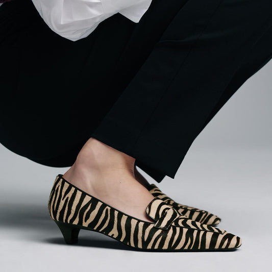 The Sigrid - Tan Zebra Haircalf low-heeled loafers worn with black trousers.