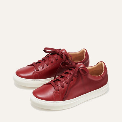 The Sneaker - Burgundy Calf by margaux-development: a pair of low-top burgundy leather sneakers with matching laces and white rubber soles, displayed side by side on a plain light background.
