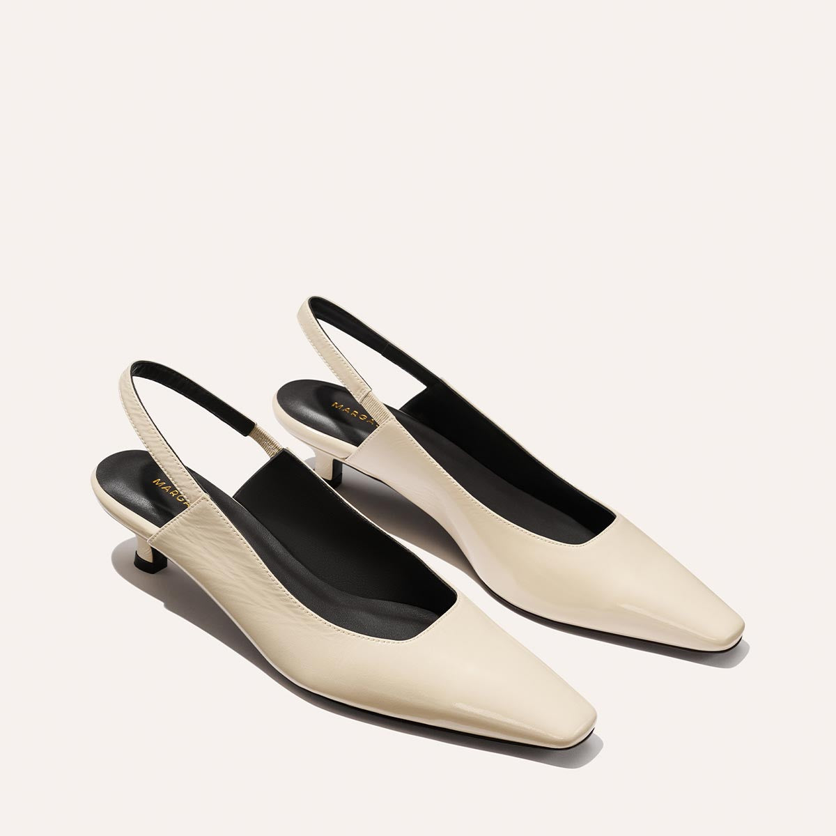 The Sofia Sling - Ecru Crinkle Patent by Margaux features elegant cream slingback heels with a chic snip toe, black insoles, and low micro heels, beautifully set against a light background.