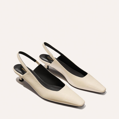 The Sofia Sling - Ecru Crinkle Patent by Margaux features elegant cream slingback heels with a chic snip toe, black insoles, and low micro heels, beautifully set against a light background.