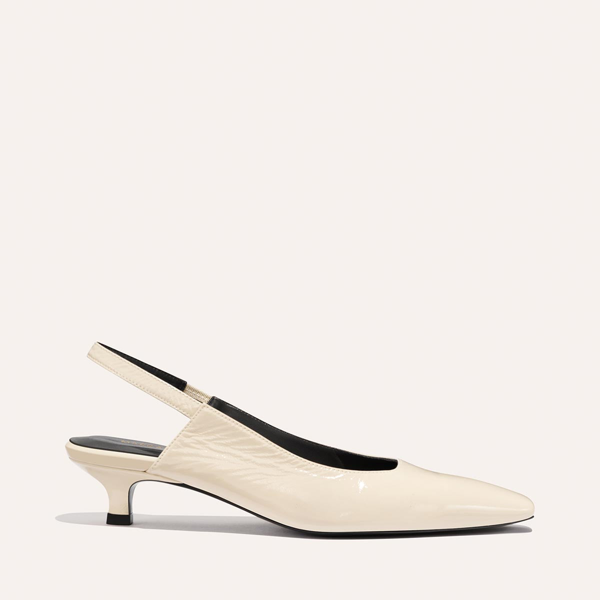 The Margaux "Sofia Sling - Ecru Crinkle Patent" is a single beige patent leather slingback pump with a low micro heel, pointed snip toe, black interior, shown on a plain light background.
