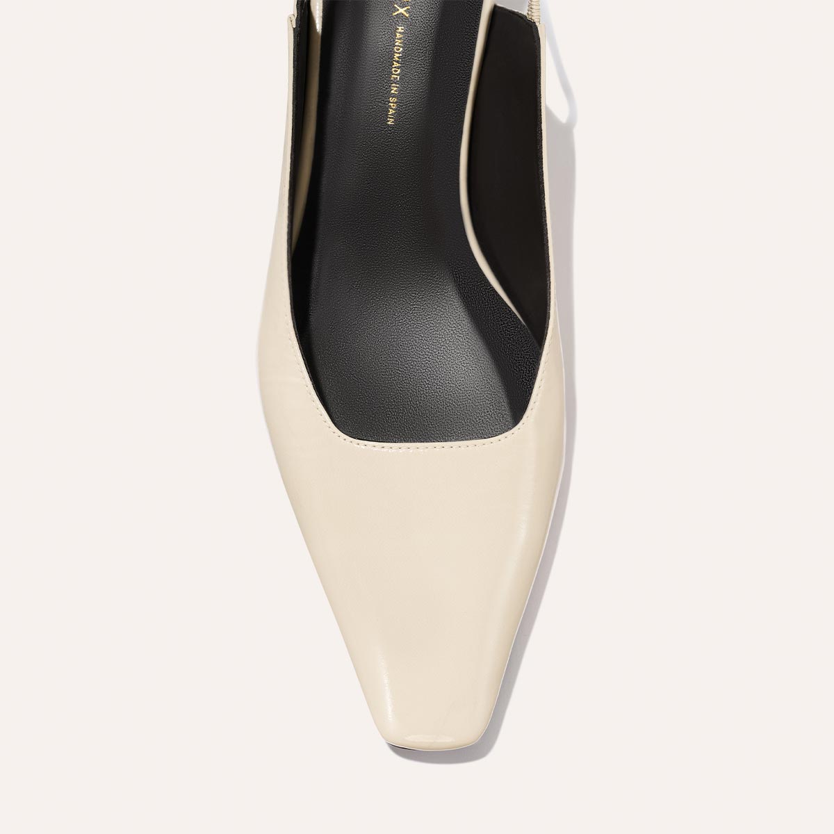 A top view of Margaux's The Sofia Sling - Ecru Crinkle Patent, a cream-colored, square-toe slingback with a black insole and subtle micro heel, shown against a light background.
