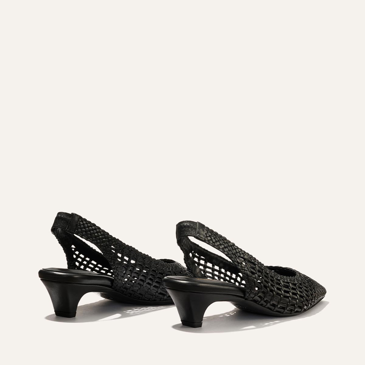 The Sofia Sling by Margaux in black woven leather features low, curved heels and pointed toes. Displayed against a plain light background, the shoes are angled to show the back and sides.