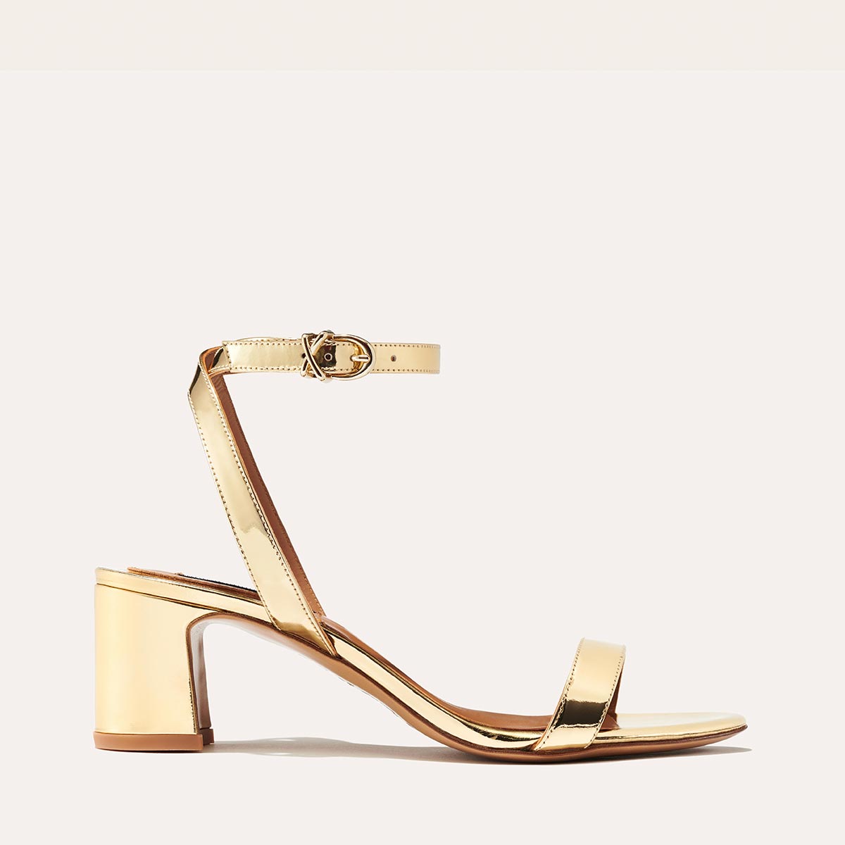 Margaux's classic and comfortable Stella Sandal in metallic gold patent leather with a perfectly placed strap and a walkable block heel
