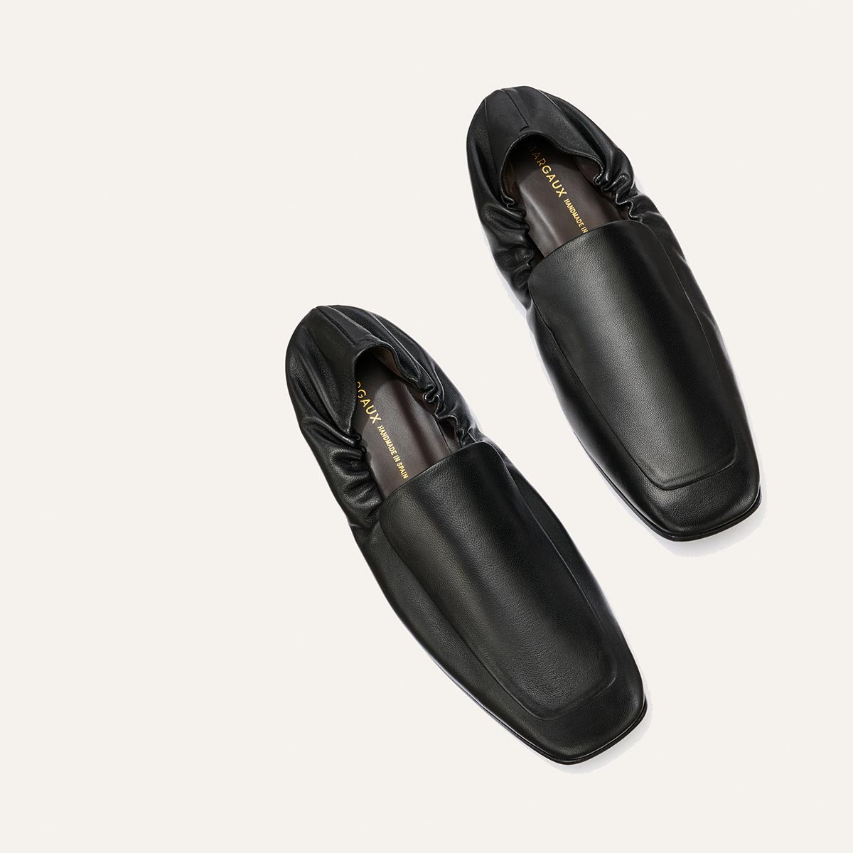 A pair of Margaux The Studio Loafer - Black Nappa, featuring black leather, square toes, and elasticized backs, displayed on a plain white background.