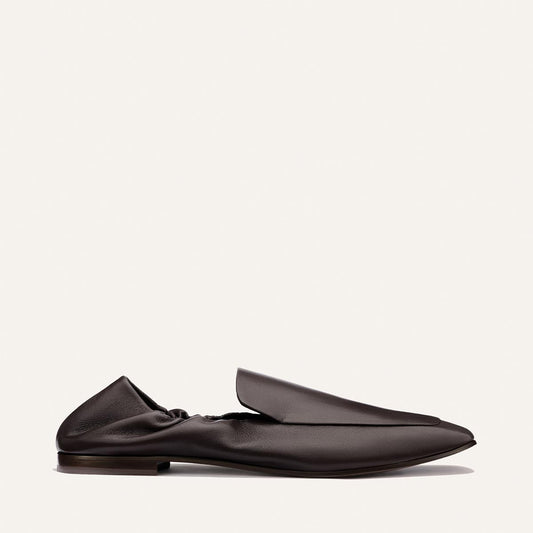 A side view of The Studio Loafer - Espresso Nappa by Margaux, a single dark brown leather slip-on featuring a slightly wrinkled texture, flat sole, and a minimalist, modern design on a plain light background.