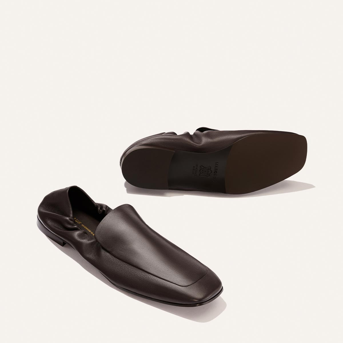A pair of Margaux's The Studio Loafer in Espresso Nappa, with one shoe upright and the other on its side to reveal the sole, displayed against a plain light background.