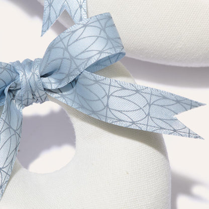 Close-up of a white Canvas Shoe Shaper with a smooth texture, featuring a blue ribbon tied in a bow with a subtle geometric pattern. This packable accessory for girls showcases Margaux’s signature elegance at its round opening.