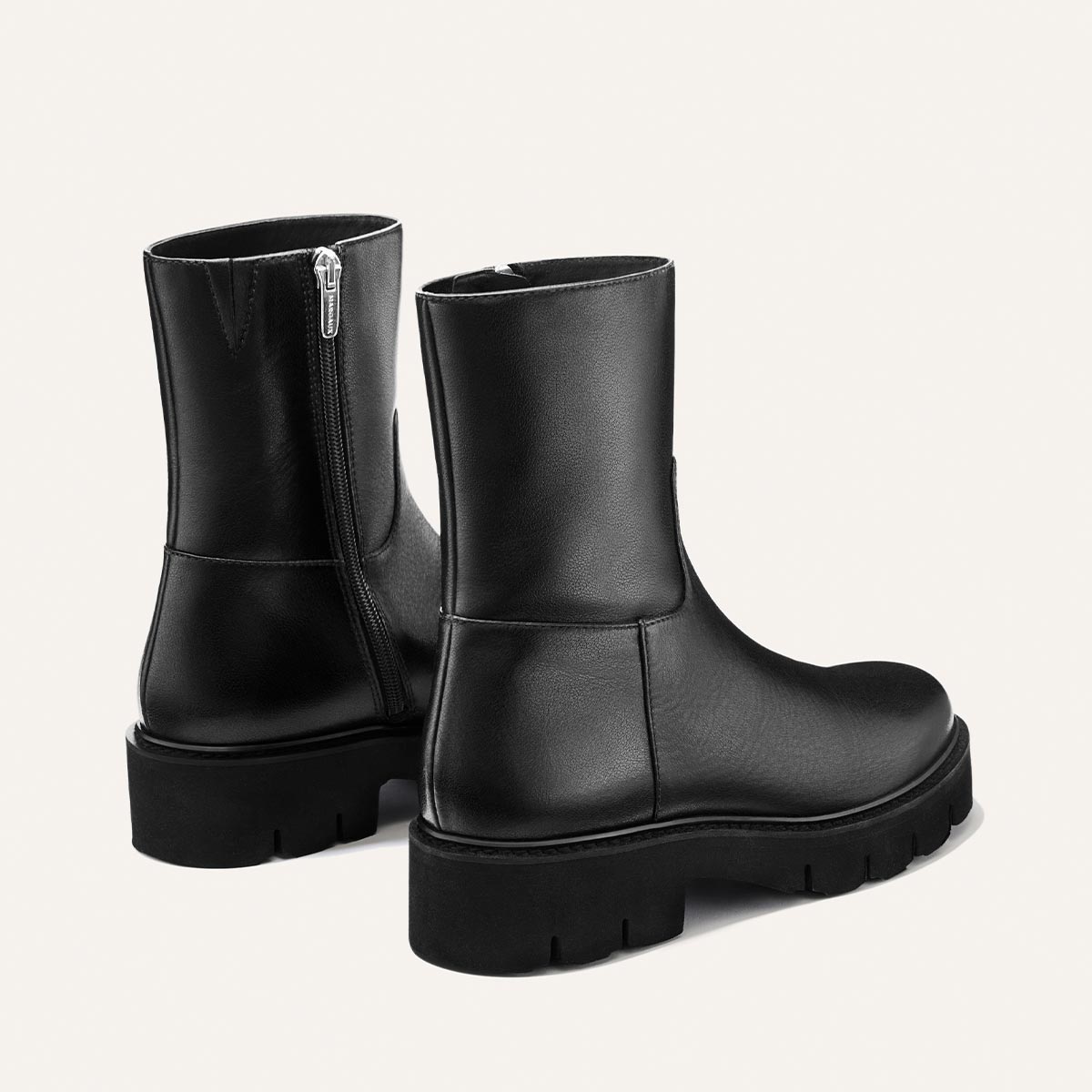 The Wells Boot - Black Calf by Margaux: a pair of black leather ankle boots featuring chunky soles and convenient side zippers, showcased against a simple, light background.
