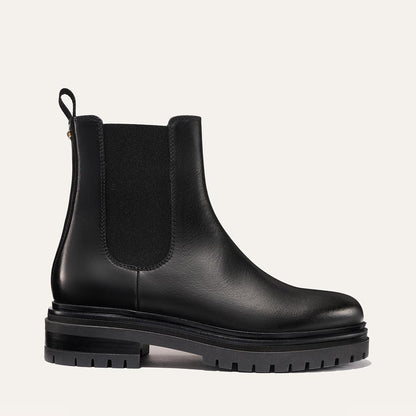 The West Chelsea Boot - Black Calf by margaux-development features black leather, elastic side panels, a back pull tab, and a thick lug sole, shown on a plain light background.
