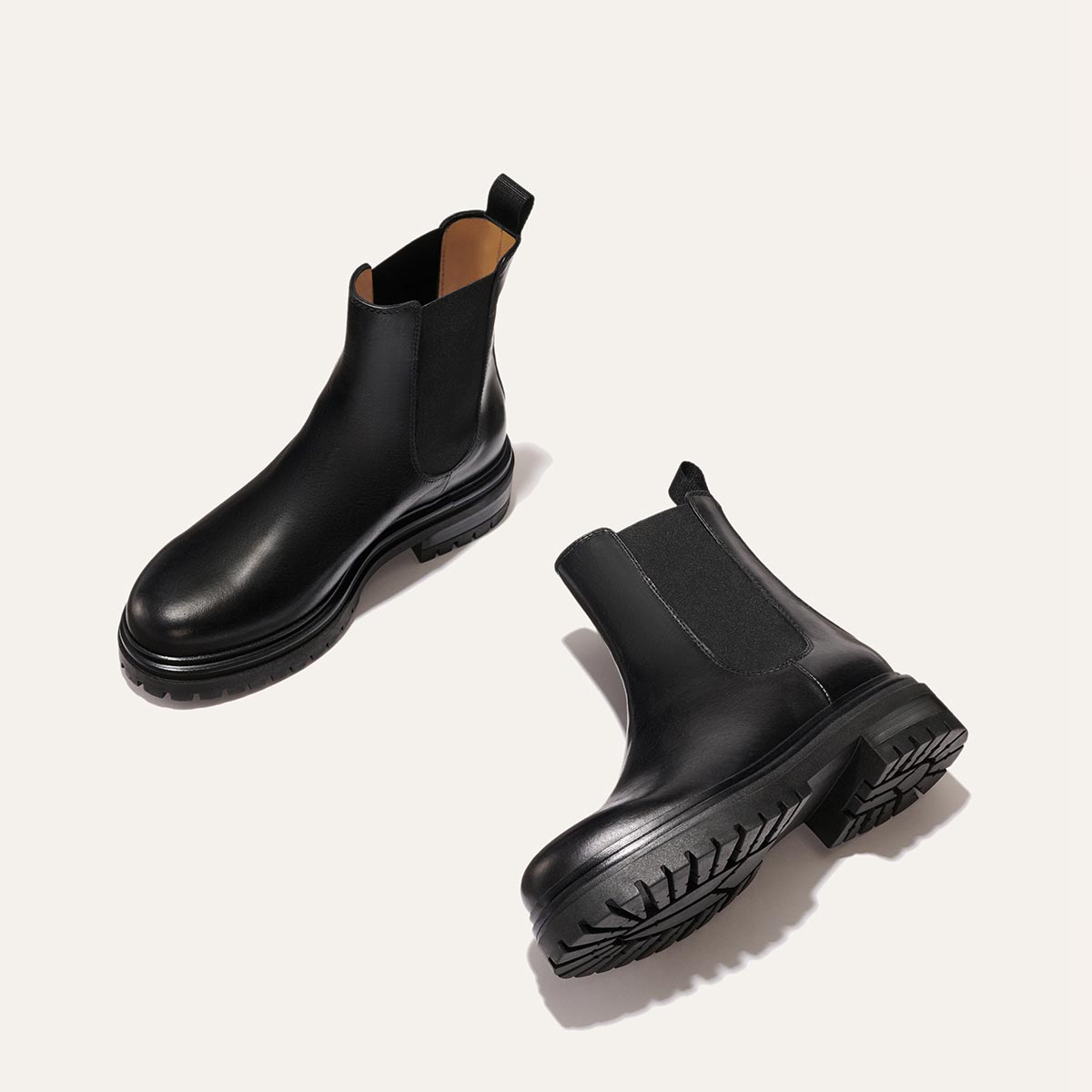 The West Chelsea Boot - Black Calf by margaux-development features black leather, elastic side panels, and thick lug soles, displayed on a light beige background.
