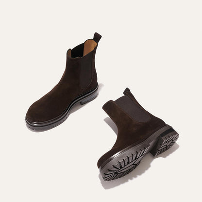 The West Chelsea Boot - Cocoa Suede by margaux-development features dark brown, water-resistant suede with black elastic panels and thick lug soles. Shown on a light background, one boot stands upright while the other lies on its side.