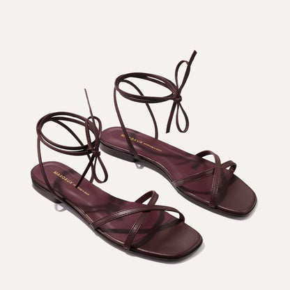 The Wrap Sandal - Burgundy Nappa by margaux-development is an elegant pair of handcrafted Spanish leather sandals in dark burgundy, with ankle wrap ties, square toes, and thin cross straps, shown on a light background.