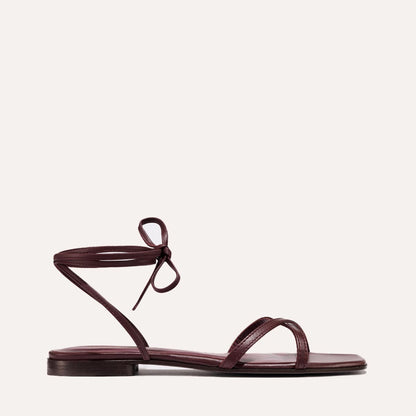 The Wrap Sandal - Burgundy Nappa by margaux-development is an elegant handcrafted Spanish leather sandal with a thin ankle tie and single toe strap, highlighted by its minimalist design on a light background.