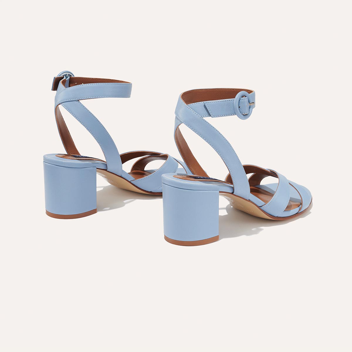 The City Sandal - Fog Nappa by margaux-development: light blue, open-toe block heels with crisscross straps and ankle buckles, cushioned insoles for comfort, shown from the back on a white background.