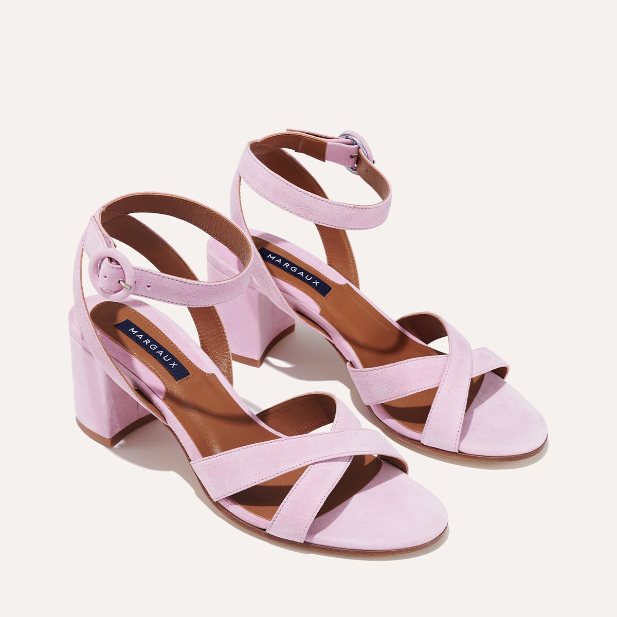 The City Sandal - Wisteria Suede by margaux-development features light pink suede, block heels, ankle straps, crisscross toe straps, and a cushioned insole with a dark blue label. Displayed on a light background.