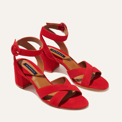 The City Sandal - Poppy Suede by margaux-development features bright red crisscross and ankle straps with round buckles, chunky block heels, a cushioned insole for comfort, and a blue Margaux label on the tan footbed.