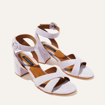 The City Sandal - Lilac Suede by margaux-development features light lavender suede, block heels, crisscross and adjustable ankle straps with round buckles, and a cushioned insole for comfort, shown on a light background.