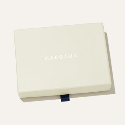 A rectangular, cream-colored box from Margaux Dev features MARGAUX in white capitals on the lid and a dark blue ribbon tab at the bottom—perfect for presenting The Physical Gift Card.