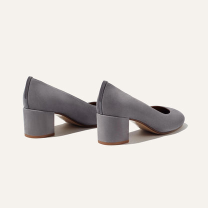 Margaux’s The Heel in Steel Suede features elegant grey suede, rounded toes, and a comfortable block heel—timeless pumps shown on a light background, positioned with heels apart.