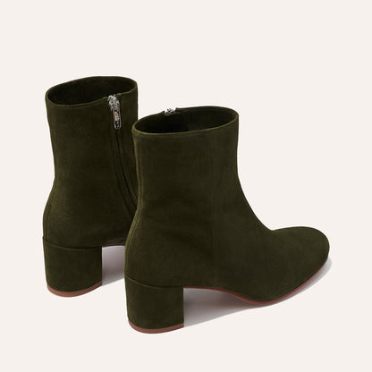 The Boot - Olive Suede by Margaux is an elegant pair of olive green suede ankle boots with block heels, almond toes, and side zippers, showcased against a plain light background.