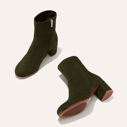 The Margaux "The Boot - Olive Suede" features elegant almond toes, block heels, side zippers, and brown soles. Displayed on a neutral background: one stands upright while the other lies on its side.
