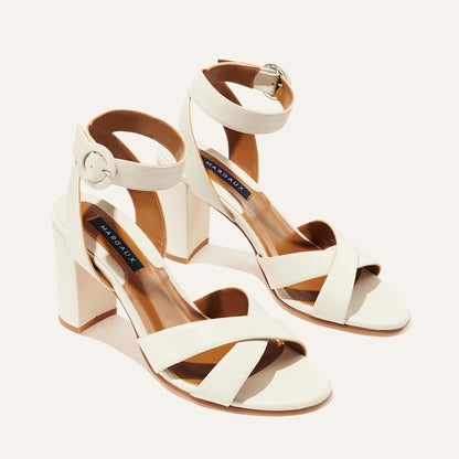 The Uptown Sandal - Ivory Nappa by margaux-development features white open-toe heels with ankle straps and thick block heels. A dark insole label with white text adds style, making these comfortable sandals perfect for any occasion.