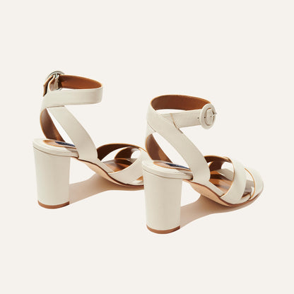 The Uptown Sandal - Ivory Nappa by margaux-development: white sandals with ankle straps and round buckles, shown from the back and side on a light background—perfect for comfort at any formal event.