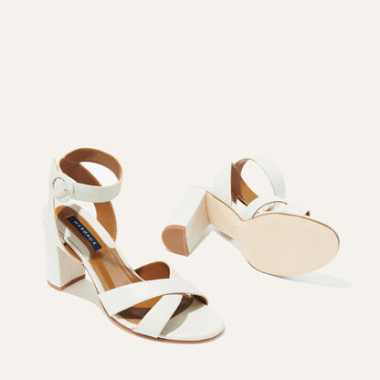 A pair of The Uptown Sandal - Ivory Nappa by margaux-development, featuring block heels, ankle straps, and buckle closures—one upright and one on its side to show the sole. A chic, comfortable choice for any formal occasion.