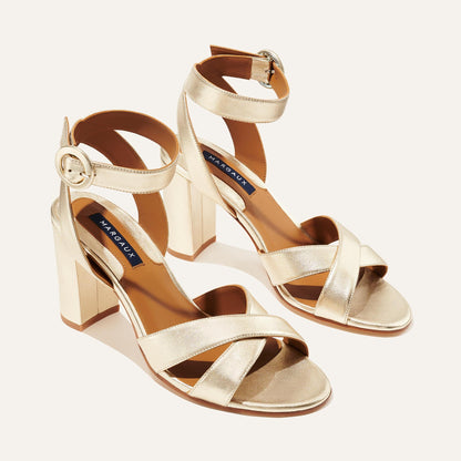 The Uptown Sandal - Champagne by margaux-development features gold crisscross and ankle straps with round buckles, designed for all-day comfort and shown on a light background.
