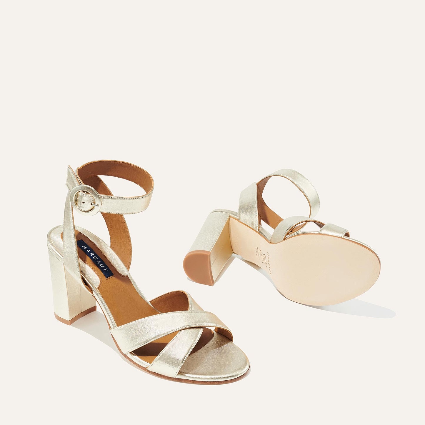 The Uptown Sandal - Champagne by margaux-development features chic gold strappy high heels with ankle straps and block heels; one shoe stands upright while the other lies on its side, highlighting style and all-day comfort.