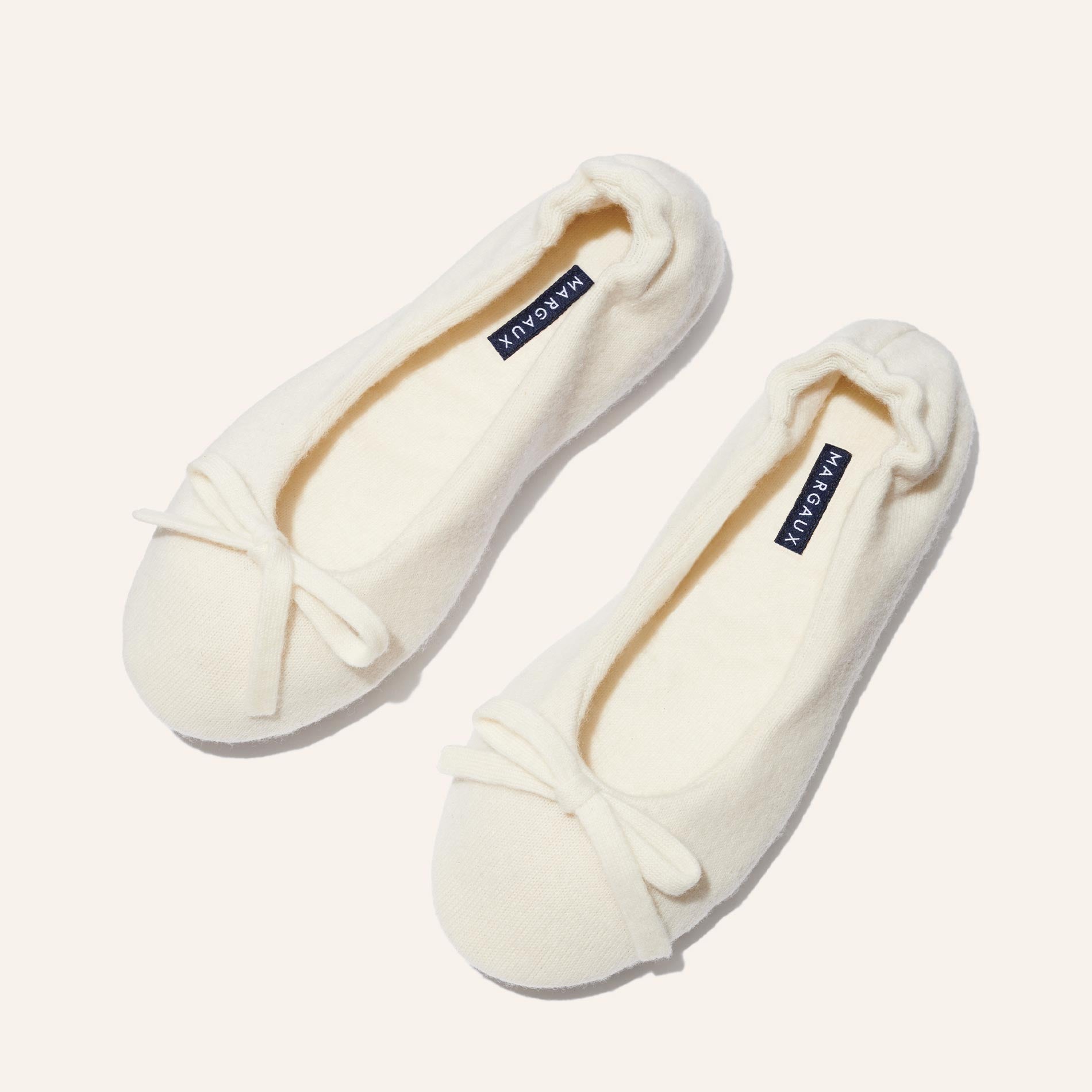 The Ballet Slipper - Ivory by Margaux: cozy cream-colored wool-cashmere flats with bows and MAROAKY labels, displayed on a light background. Perfect for relaxing in style.