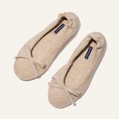 The Ballet Slipper - Oatmeal by Margaux features cozy beige ballet flats in soft, textured fabric with delicate toe bows and navy blue Margaux insoles—perfect for relaxing in style, elegantly presented on a light background.